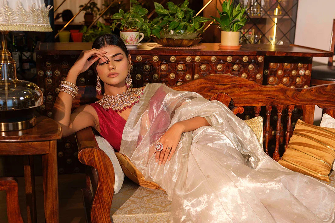 Woman in elegant white handloom saree with maroon blouse lounging on wooden bench with cushions