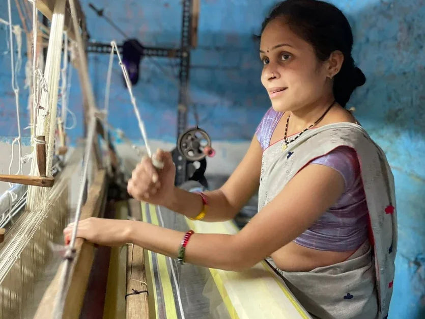 Woman in traditional saree weaving handloom fabric in a workshop with blue walls, showcasing Indian craftsmanship