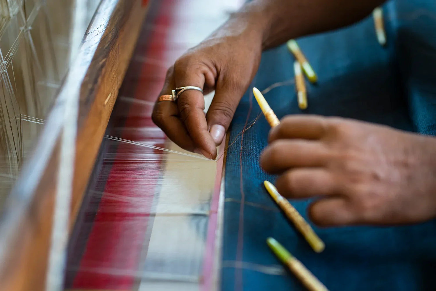 Artisan hand weaving blue silk fabric on loom with wooden weaving tools, close up